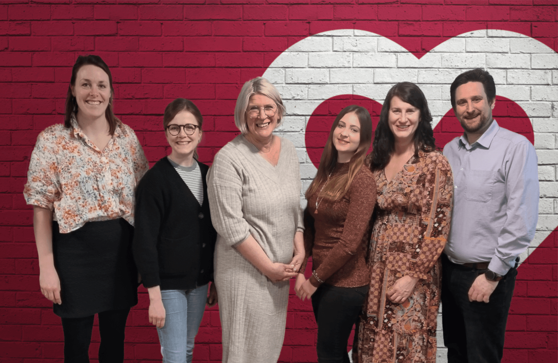 Das Team der Lotsentätigkeit steht lächelnd vor einer roten Backsteinwand mit Herzsymbol – ein engagiertes Team, das Unterstützung und Hilfe anbietet. Das Team der Lotsentätigkeit steht lächelnd vor einer roten Backsteinwand mit Herzsymbol – ein engagiertes Team, das Unterstützung und Hilfe anbietet.