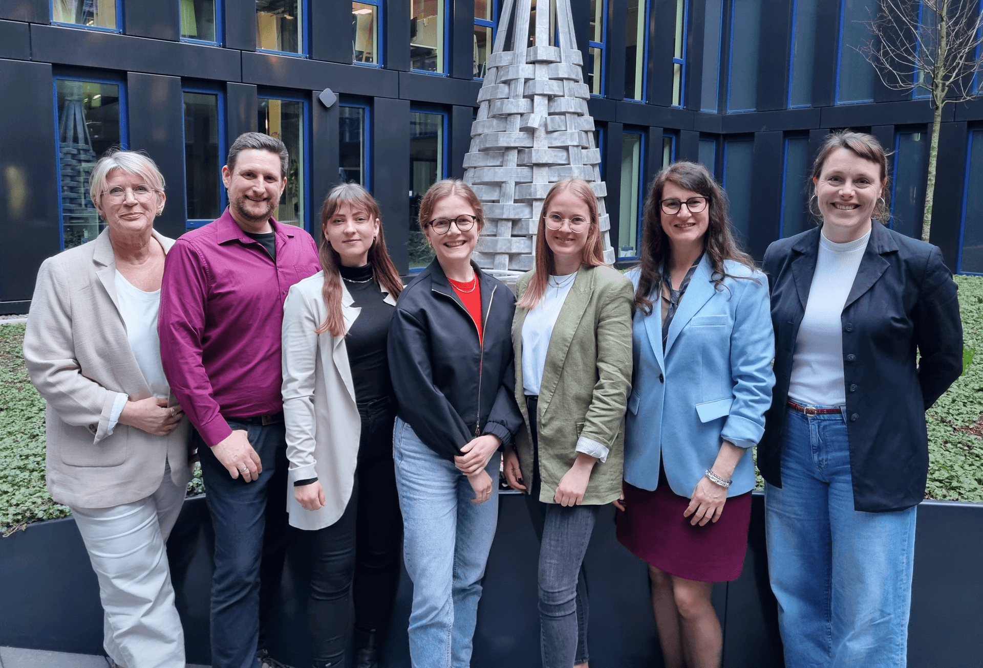 Das Team der Lotsentätigkeit steht lächelnd vor einer Metalskulptur – ein engagiertes Team, das Unterstützung und Hilfe anbietet. Das Team der Lotsentätigkeit steht lächelnd vor einer Metalskulptur – ein engagiertes Team, das Unterstützung und Hilfe anbietet.