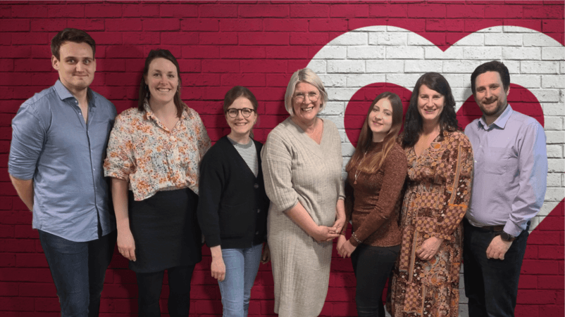 Das Team der Lotsentätigkeit steht lächelnd vor einer roten Backsteinwand mit Herzsymbol – ein engagiertes Team, das Unterstützung und Hilfe anbietet. Das Team der Lotsentätigkeit steht lächelnd vor einer roten Backsteinwand mit Herzsymbol – ein engagiertes Team, das Unterstützung und Hilfe anbietet.